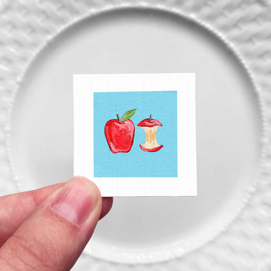 A hand is holding a small square with an illustration of an apple and an apple core on it.
