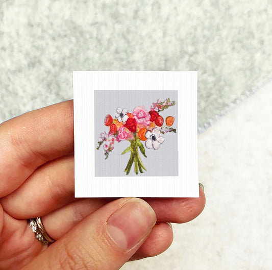 A hand holding a small square card with a colorful floral design.