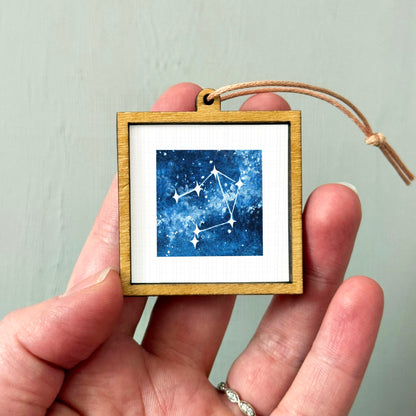 A hand holding a small wooden frame containing a framed image of a starry night sky.