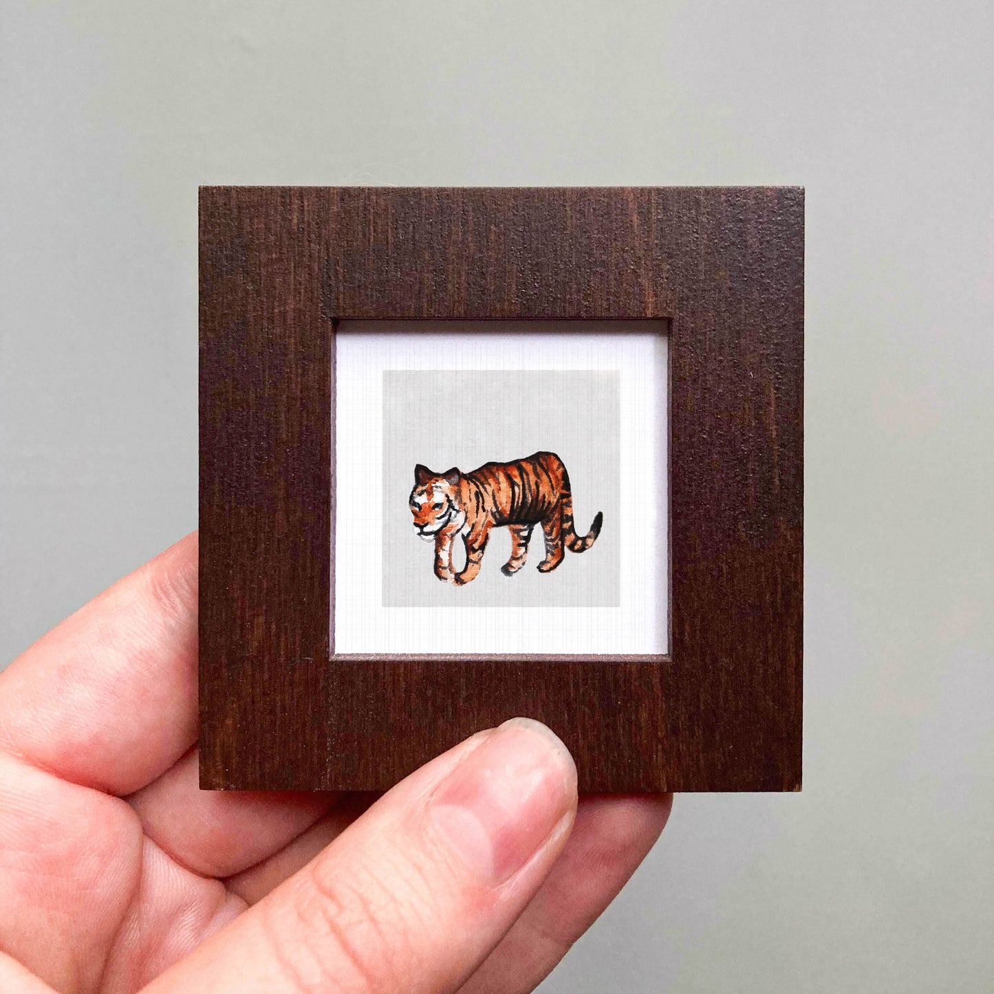A hand is holding a small wooden frame containing a picture of a tiger.