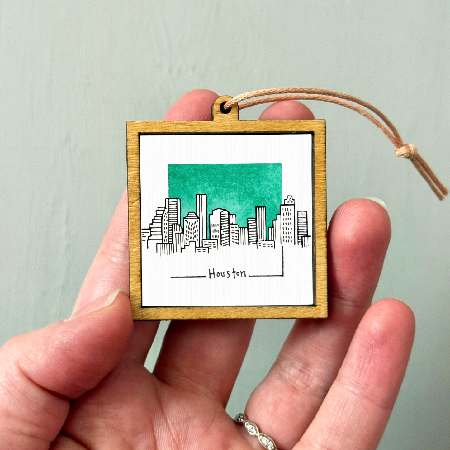 A hand holding a small wooden frame with a picture of a city skyline and the word "Houston" written on it.