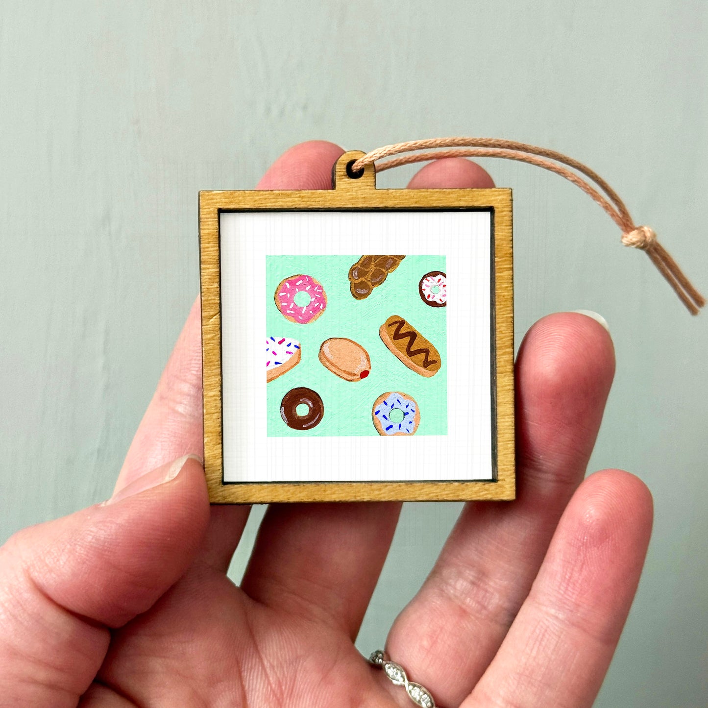 A hand holding a small wooden frame containing a picture of various donuts.