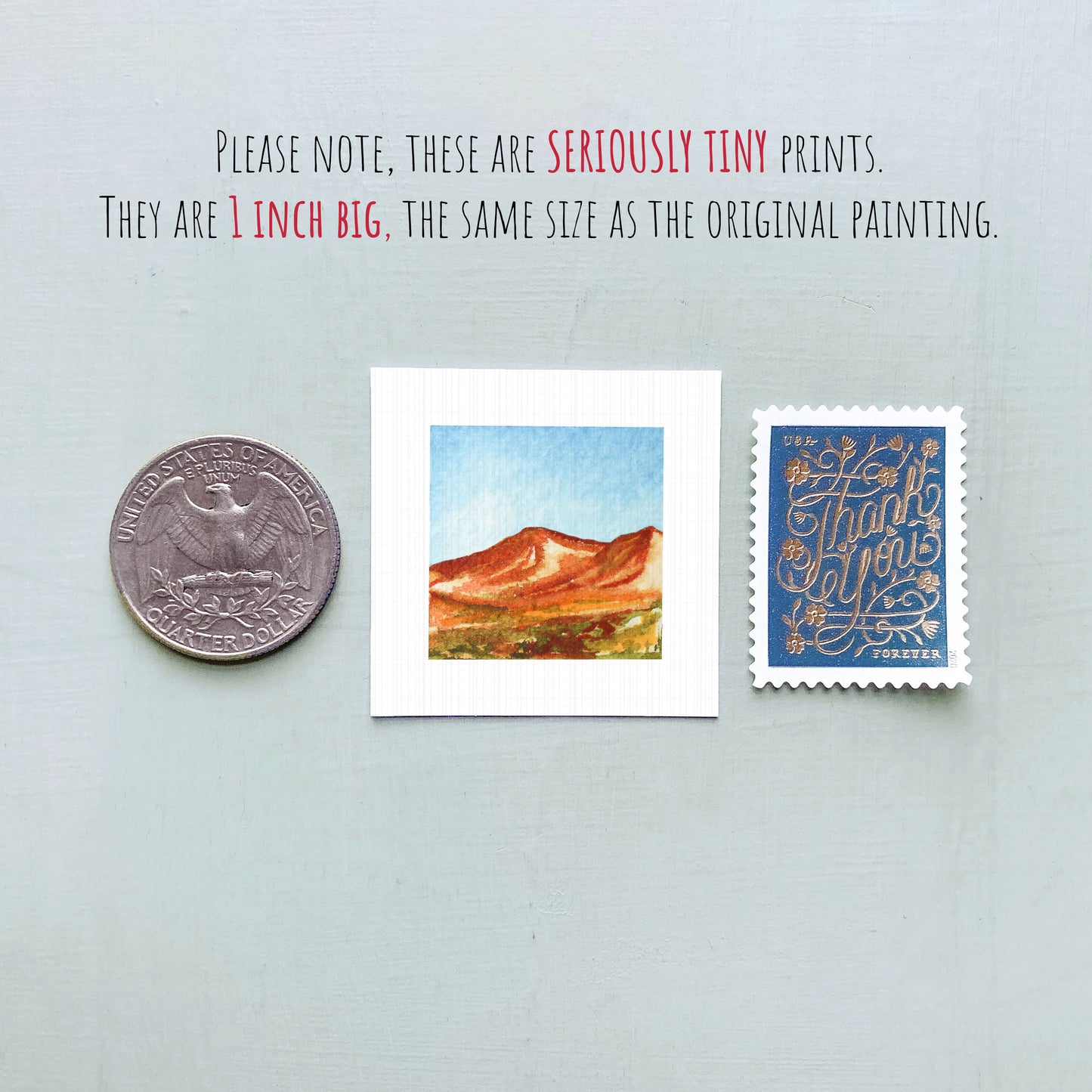 three small prints: a quarter, a square print of a mountain landscape, and a blue postage stamp with gold lettering.