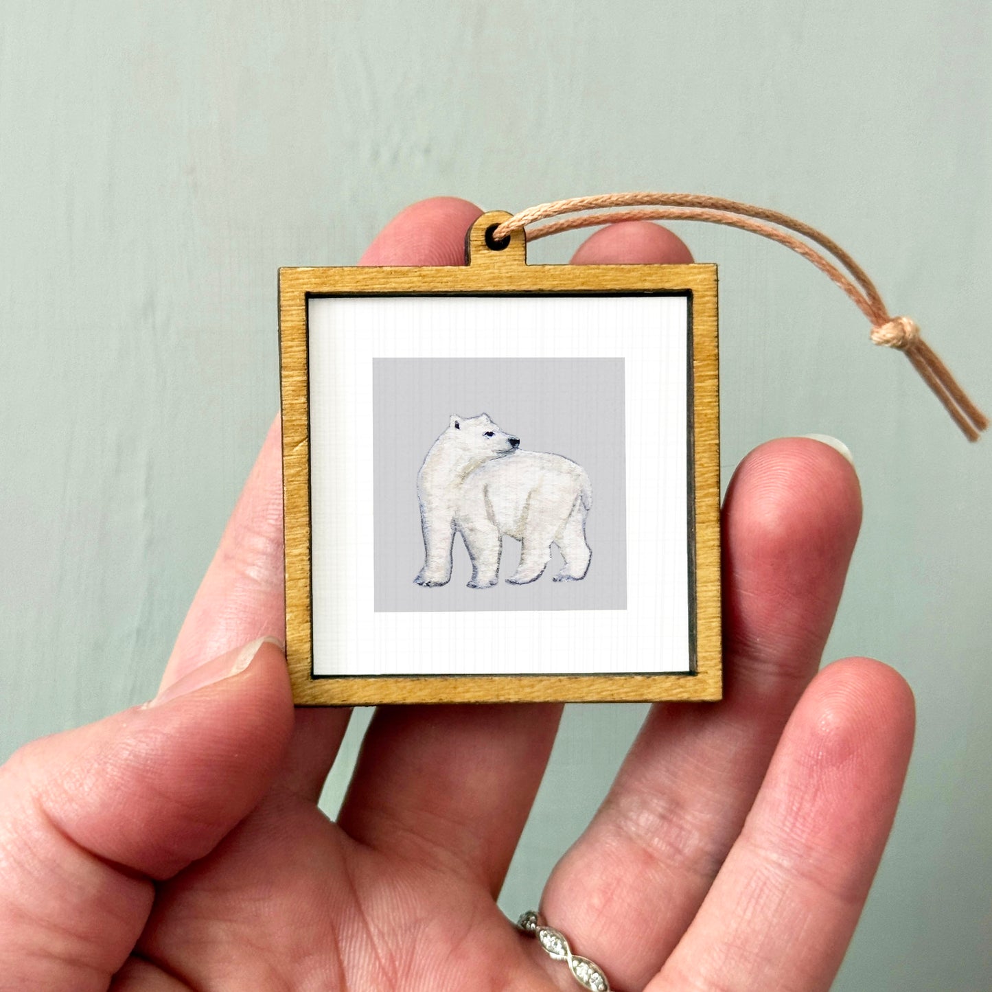 A person's hand holding a small wooden frame containing a picture of a polar bear.