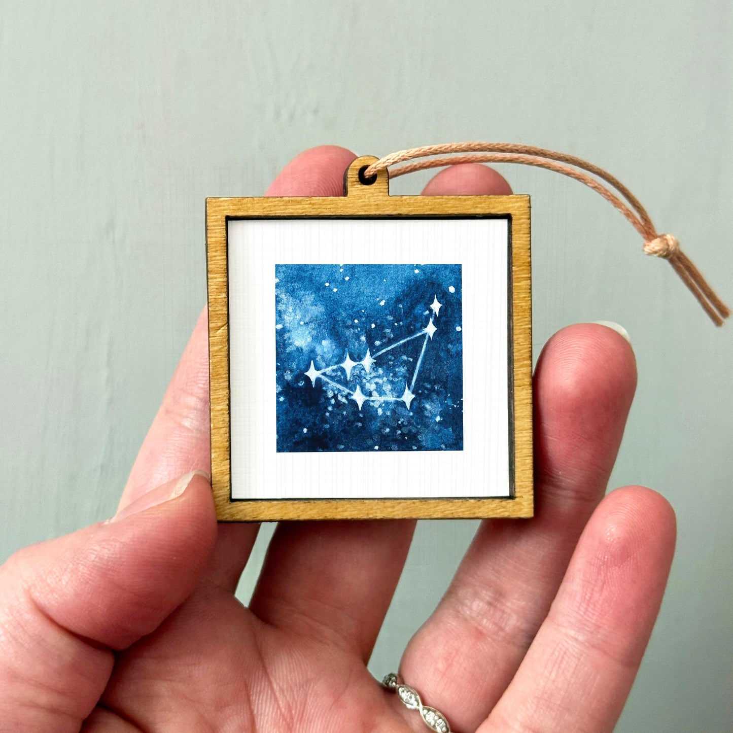 A hand holding a small wooden frame containing a framed image of a starry night sky.