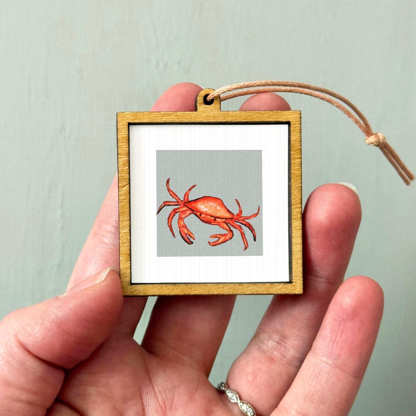 A person's hand holding a small wooden frame containing a framed image of a crab.