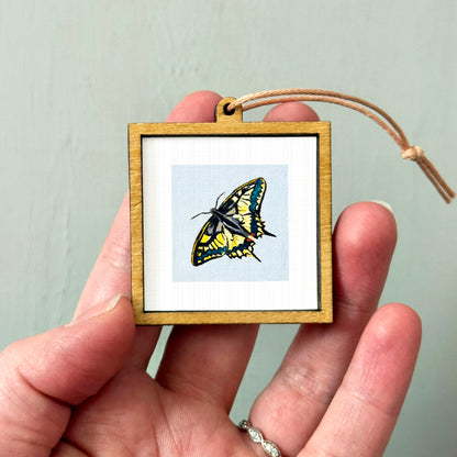 A hand holding a small wooden frame containing a picture of a colorful butterfly.