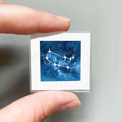 A hand is holding a small square picture of a starry night sky with a constellation.