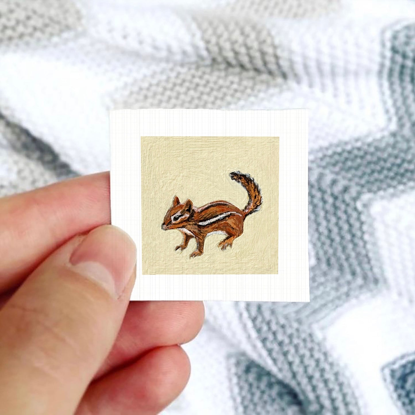 A person's hand is holding a small square card with an image of a chipmunk on it.