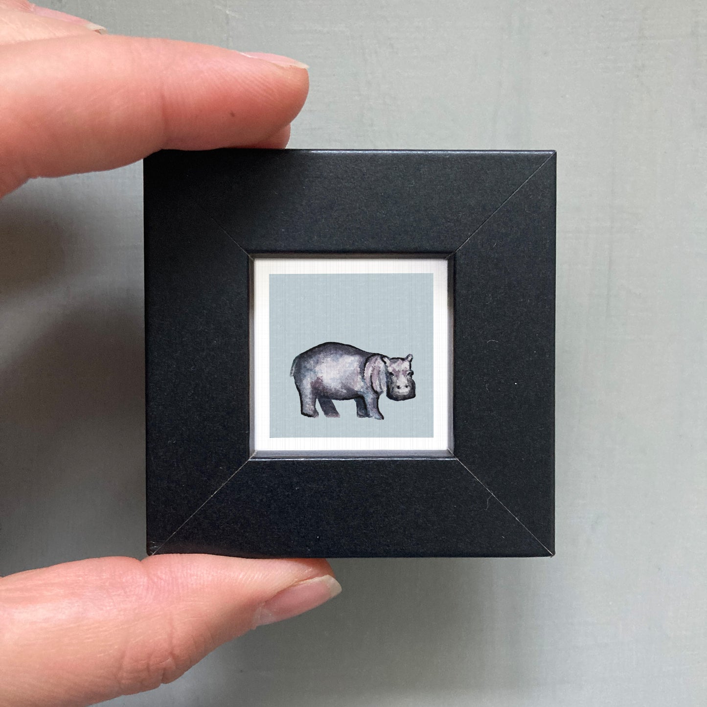 A person's hand is holding a small black square frame containing a picture of a rhinoceros.
