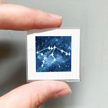 A hand is holding a small square-shaped object with a picture of a starry night sky on it.