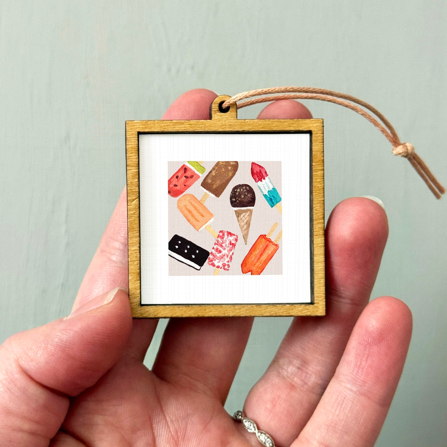 A person's hand holding a small wooden frame containing a framed image of various colorful ice cream cones.