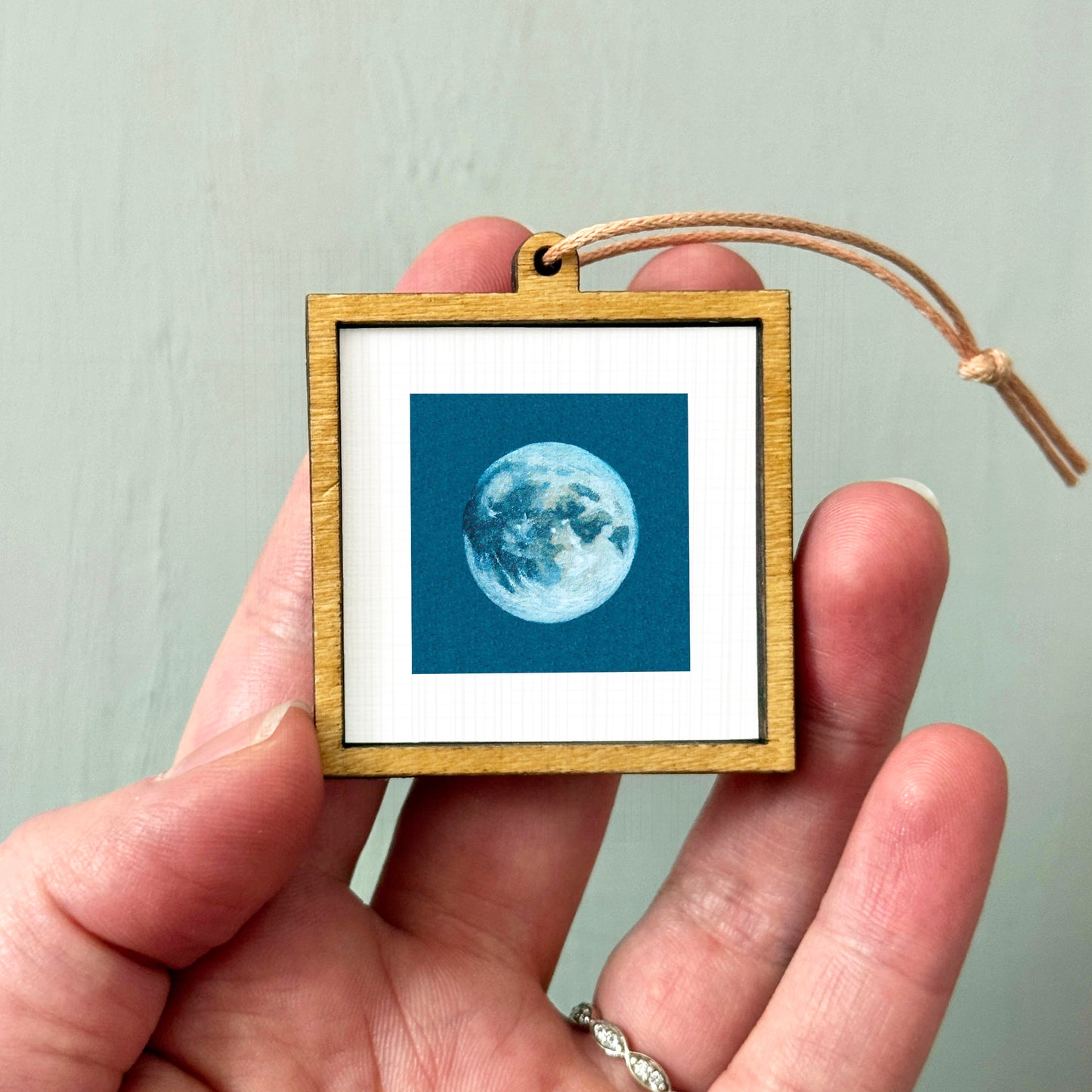 A hand holding a small wooden frame containing a framed image of a moon.