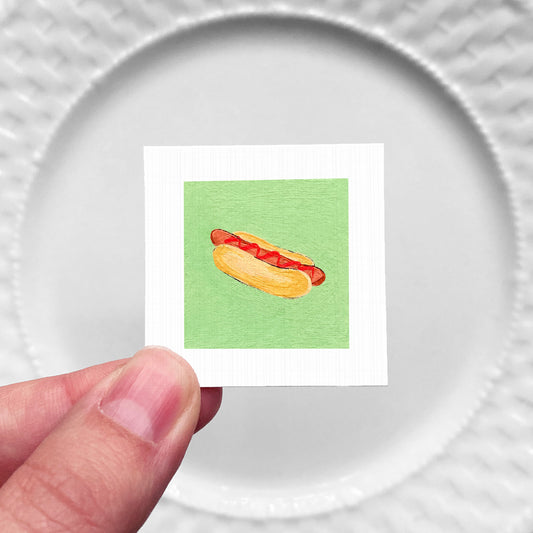 A hand is holding a small square with a picture of a hot dog on it.