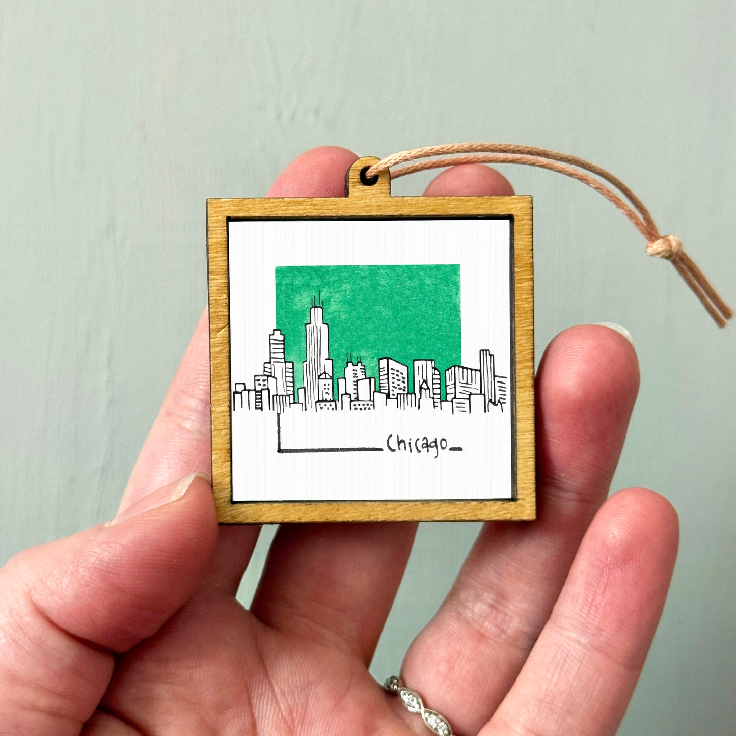 A hand holding a small wooden frame with a picture of a city skyline and the word "Chicago" written on it.