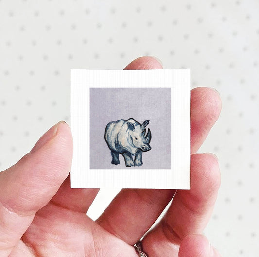 A hand holding a small square picture of a rhinoceros.