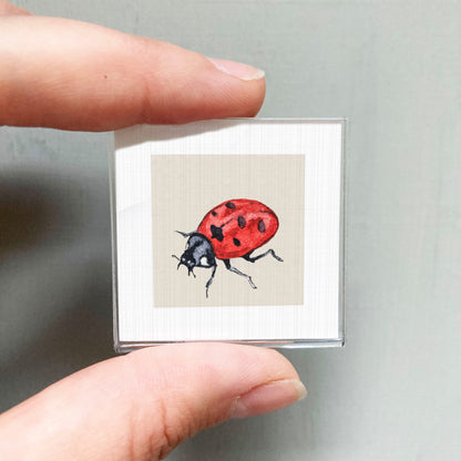 A person's hand is holding a small square picture of a red ladybug.