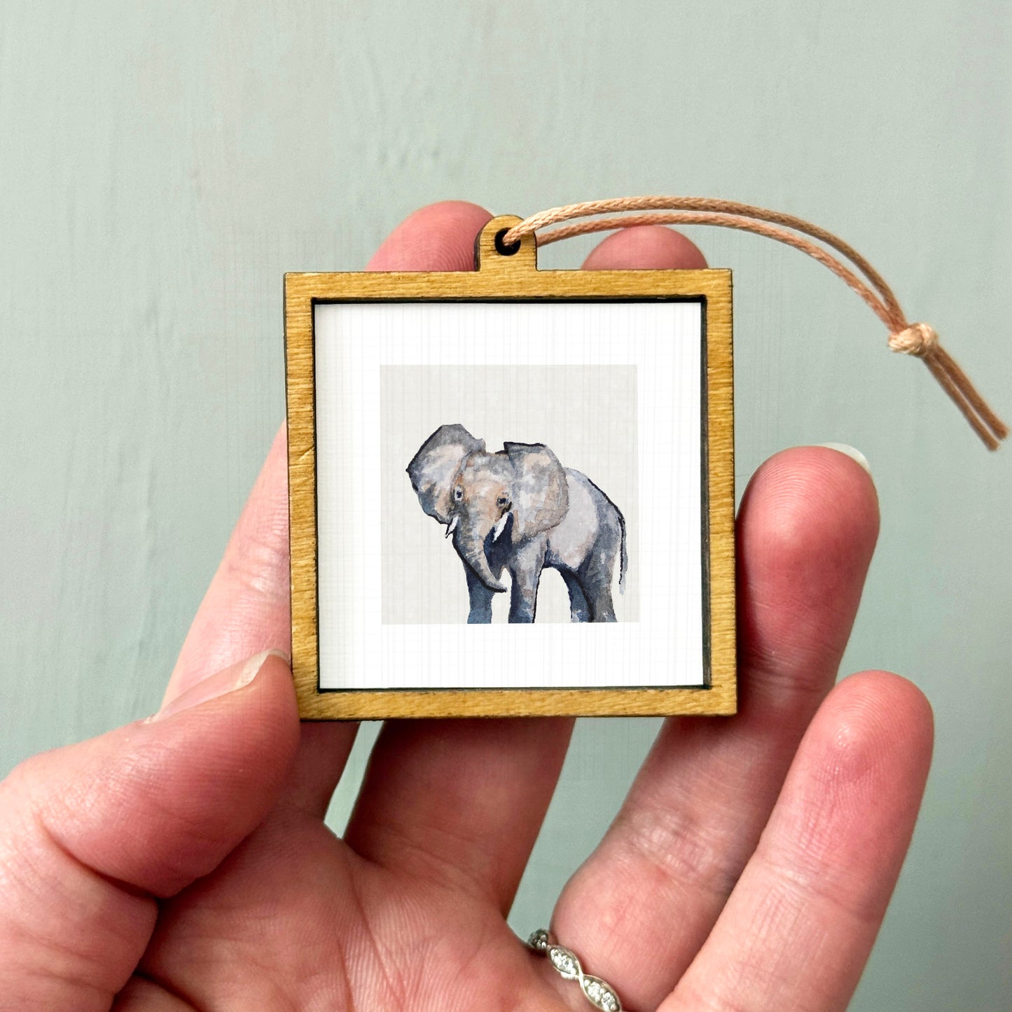 A person's hand holding a small wooden frame containing a picture of an elephant.