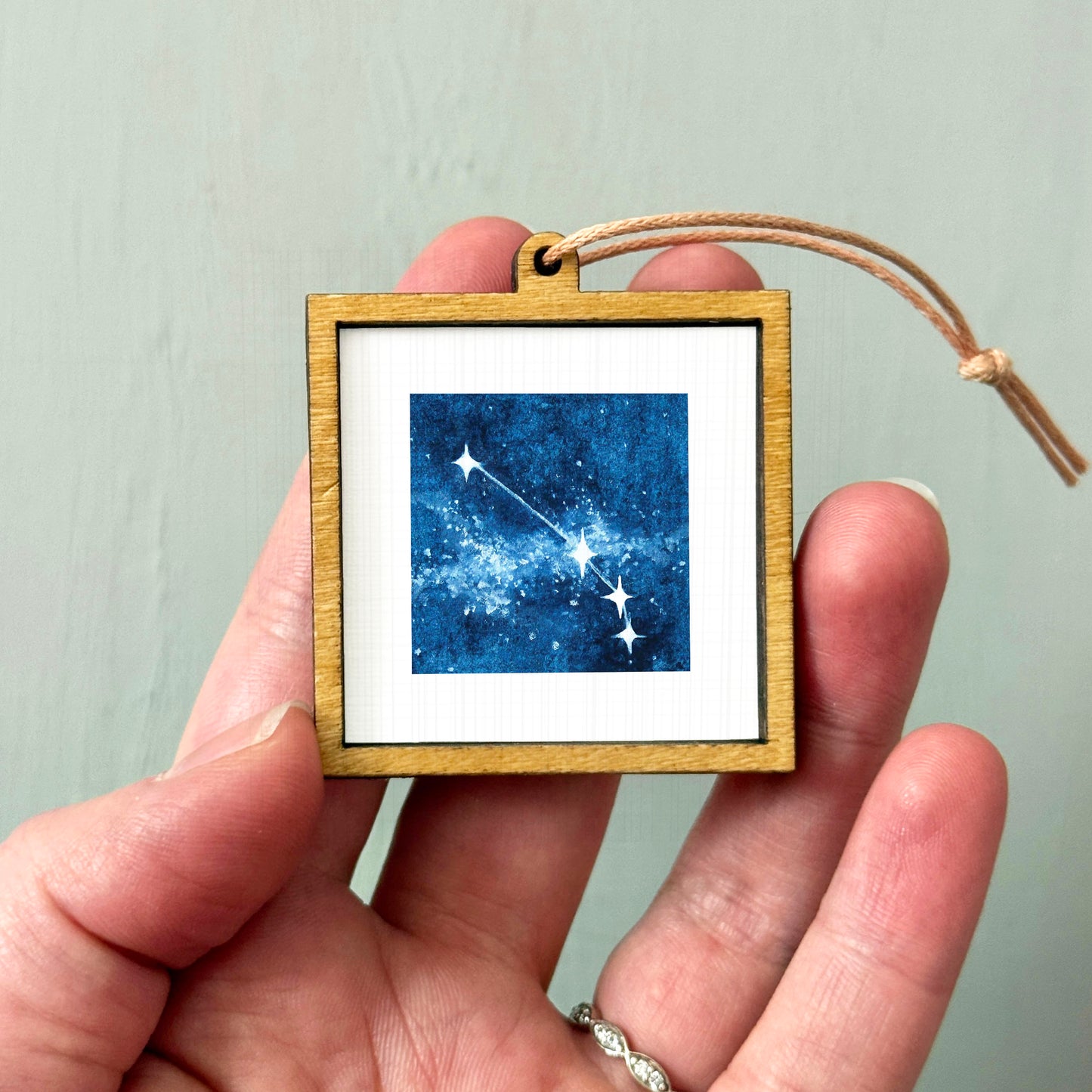 A hand holding a small wooden frame containing a framed image of a starry night sky.
